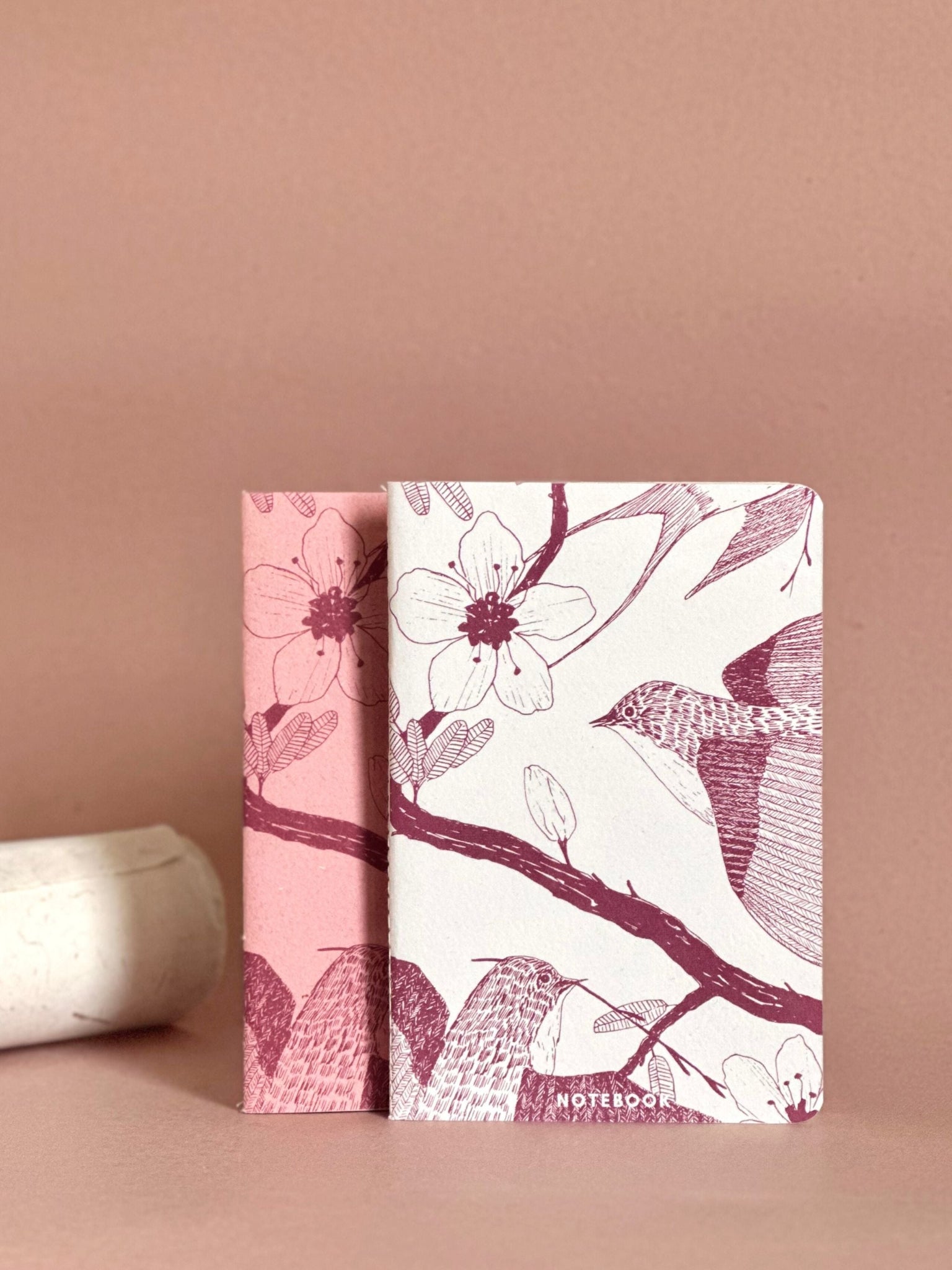 Two floral notebooks with pink and white design on a beige background